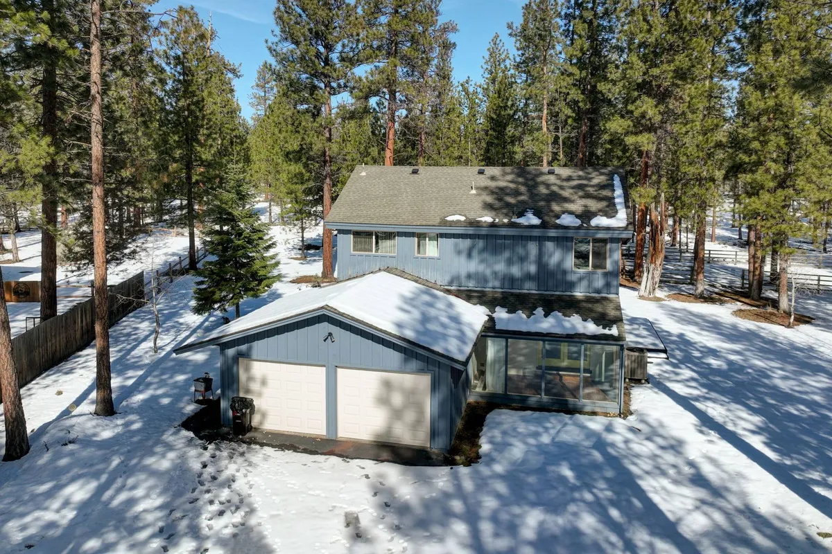 This exterior shot shows a two-story house surrounded by a snow-covered yard and tall pine trees. The scene evokes the spirit of outdoor family fun, group gatherings, and the tranquility of a community environment.