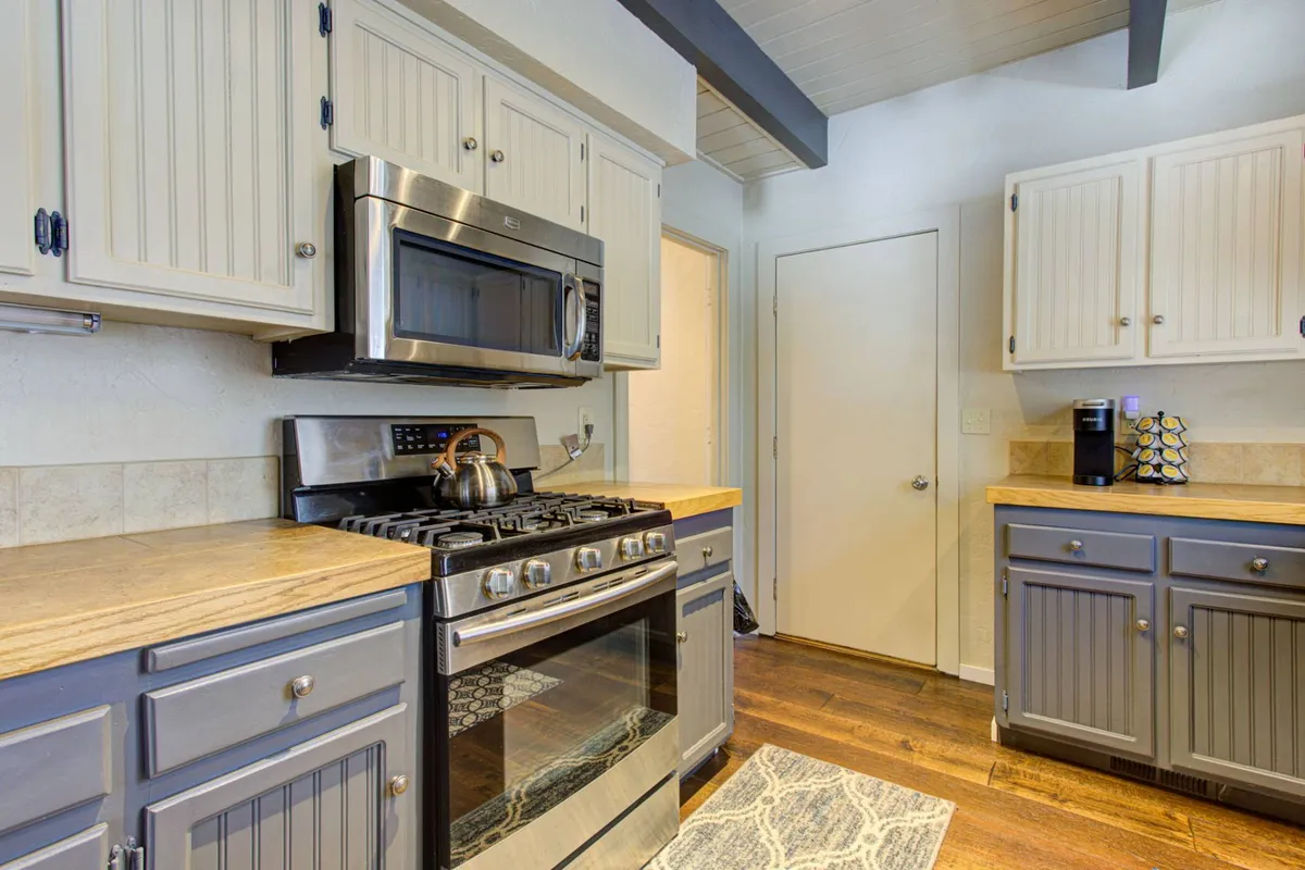 A bright kitchen view featuring gleaming stainless steel appliances, wooden countertops, and gray cabinetry. The setup is uncluttered and modern, emphasizing ample workspace and openness.