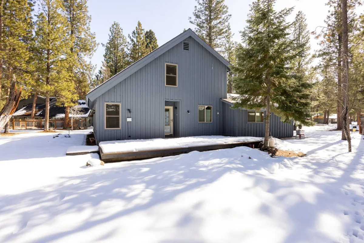A serene winter scene featuring a blue wooden exterior surrounded by snow-covered ground and tall pine trees, capturing the peaceful beauty of the forest setting. The mood is quiet and inviting, evoking cozy gatherings and winter activities like building snowmen.