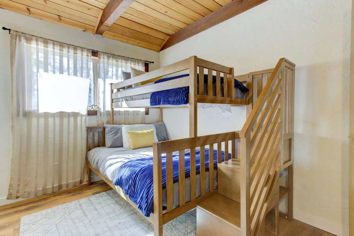 A playful yet inviting bunk room with a twin-over-full bunk bed, decorative pillows, and a window draped with sheer curtains, allowing soft daylight to filter in. The cozy space suggests both comfort and fun, ideal for children or family groups.