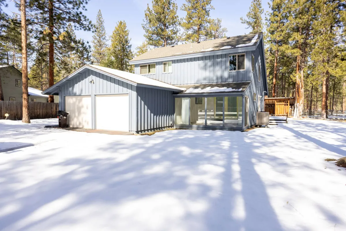 This image captures a two-story house with an attached garage, nestled among tall pine trees and surrounded by a snow-covered yard. The serene exterior setting alludes to group activities like outdoor gatherings or enjoying the natural beauty together. The home’s inviting look suggests both comfort and community, aligning with the idea of shared amenities.