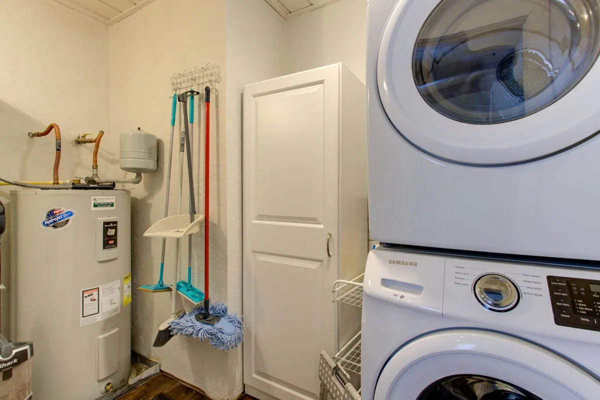 This interior image focuses on a practical laundry and storage area, featuring a washing machine, dryer, storage cabinet, and cleaning tools. The functional setup emphasizes organization and ease of transition from outdoor activities, aligning with the section's description of a gear zone and practical entryway.